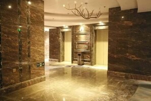 Een moderne lobby met marmeren vloeren, een centrale lift en een kroonluchter.