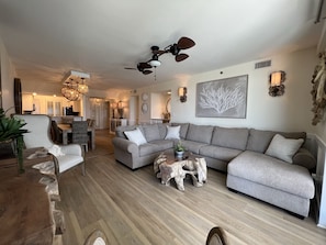 Amplia sala de estar con un sofá seccional gris, una mesa de centro de madera y un comedor con mesa y sillas de madera.
