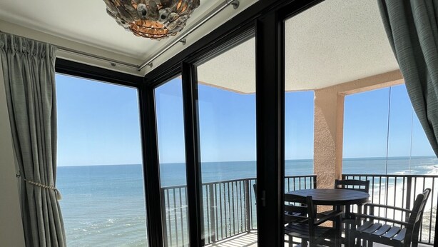 A room with a large sliding glass door leading to a balcony with a view of the sea. There is a bed with white bedding and a textured rug on the floor. - SOPHISTICATED BEACHFRONT RETREAT -  New Furniture & Decor!! (Orange Beach)