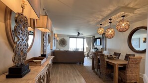 A spacious living area with a wooden floor, a sofa, a dining table with wicker chairs, and decorative wall sconces. - SOPHISTICATED BEACHFRONT RETREAT -  New Furniture & Decor!! (Orange Beach)