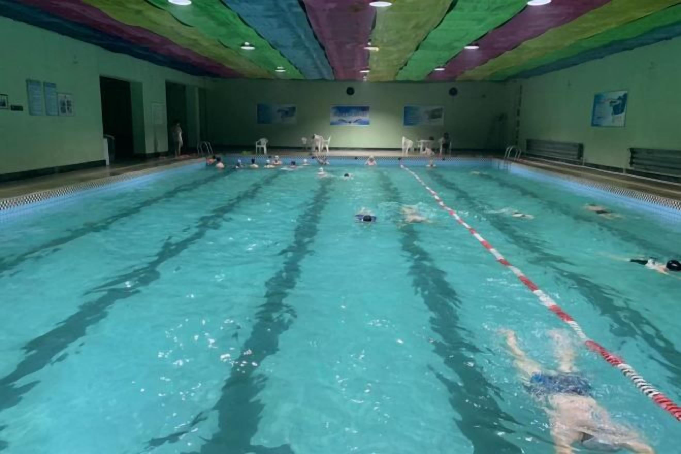 A swimming pool with lanes, a diving board, and a ceiling with colorful patterns.
