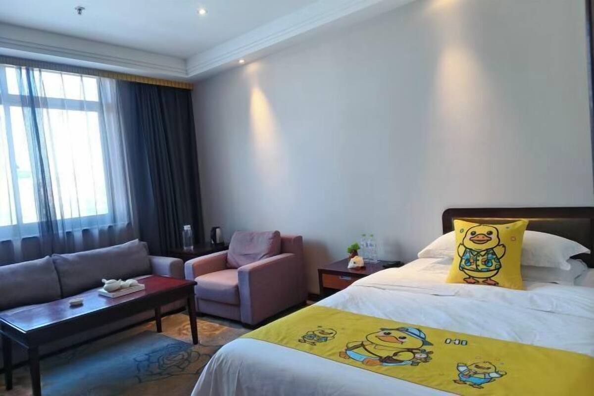 A hotel room with a bed, a sofa, a chair, a nightstand, and a window with curtains.