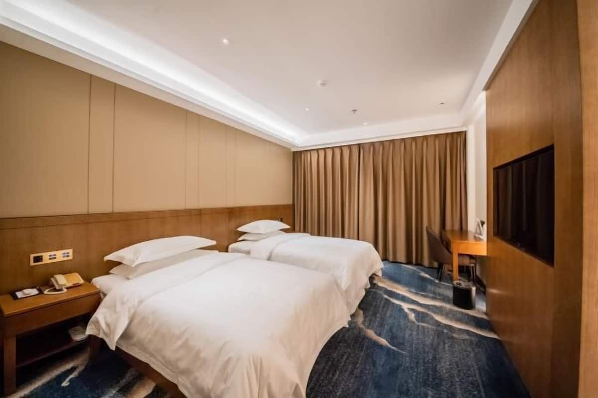 A hotel room with two beds, a wooden headboard, a desk with a chair, a telephone, and a television.
