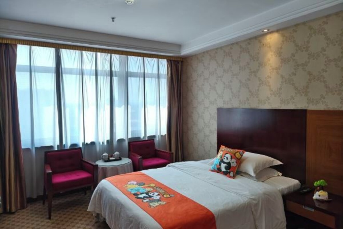 A hotel room with a large bed, two armchairs, a small table, and a nightstand.