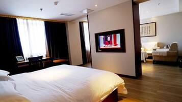 A hotel room with a large bed, a television on the wall, and a desk with a chair.