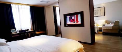 Ett hotellrum med en stor säng, en tv på väggen och ett skrivbord med en stol.
