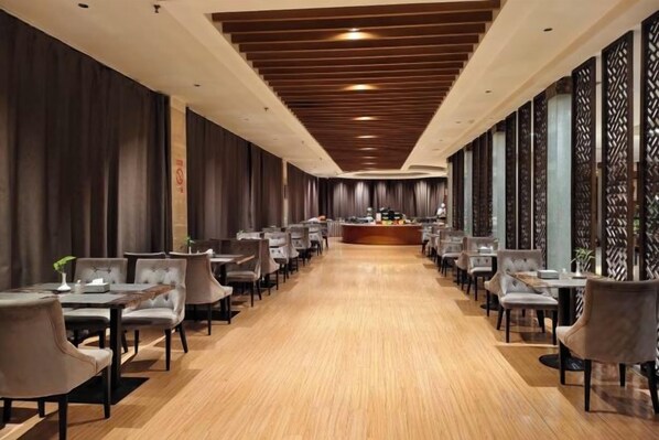 A long, narrow hotel lobby with a central reception desk, rows of tables and chairs, and a wooden floor. - Jincheng Hot Spring Hotel (Zhaoyuan)