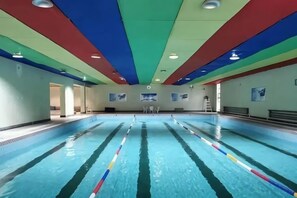 Une piscine avec des couloirs de nage, des éclairages au plafond et un escalier.
