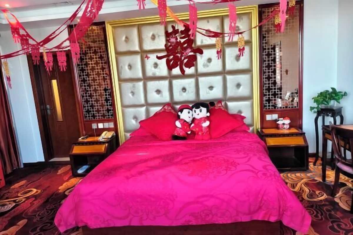 A hotel room with a large bed, a decorative headboard, a wooden nightstand, a bedside table, and a chair.