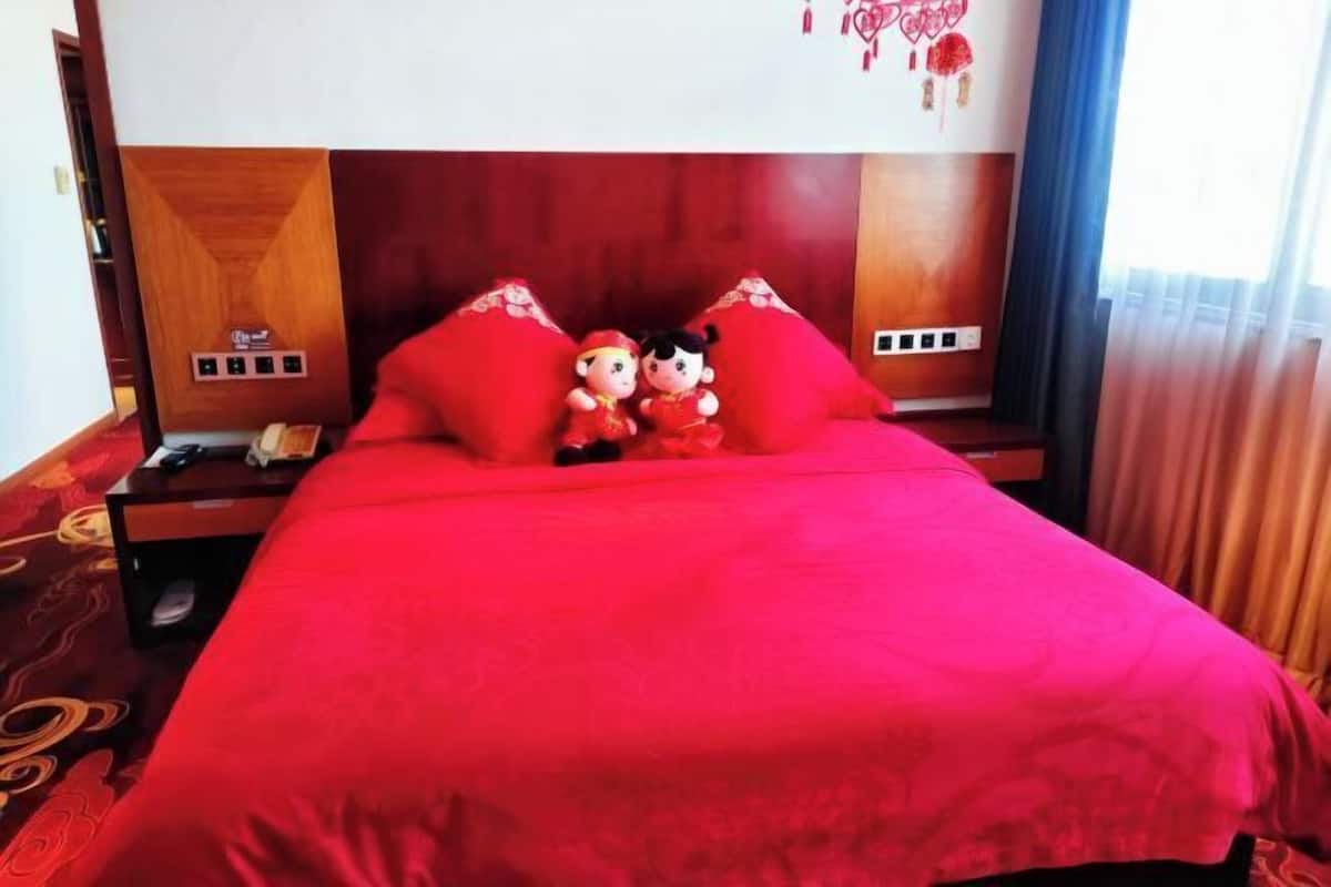 A hotel room with a wooden headboard, a red bedspread, and two plush toys on the pillows.