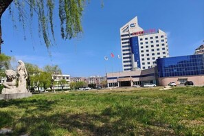 A modern building with a glass facade, a statue in the foreground, and flags in the background. - Jincheng Hot Spring Hotel (Zhaoyuan)