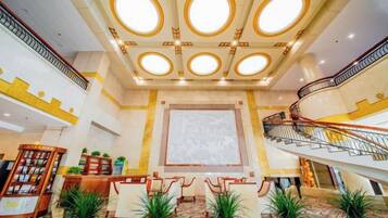 Un vestíbulo de hotel con una imponente escalera, una recepción y un amplio espacio para sentarse.