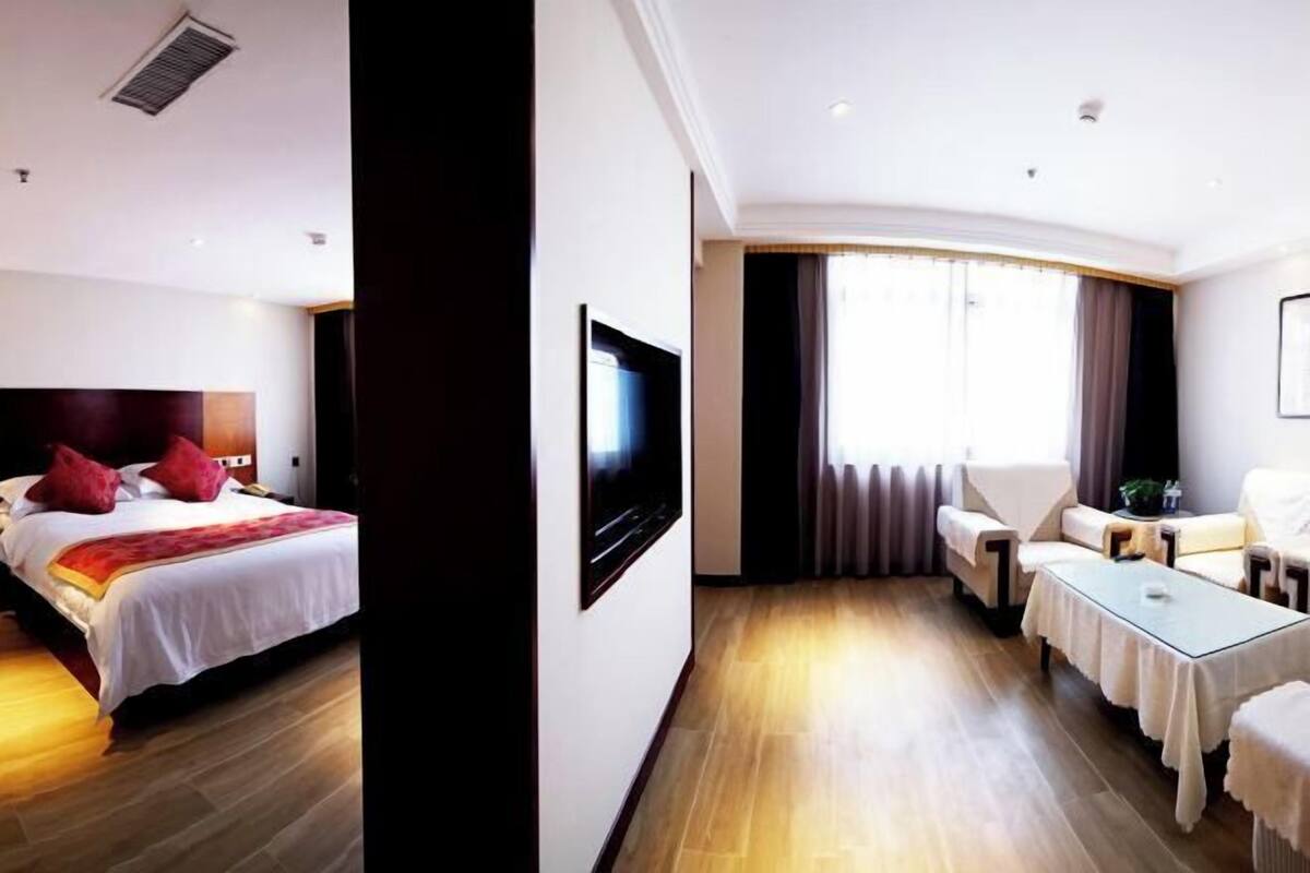 A hotel room with a bed, a TV, a seating area with a table, and a large window.
