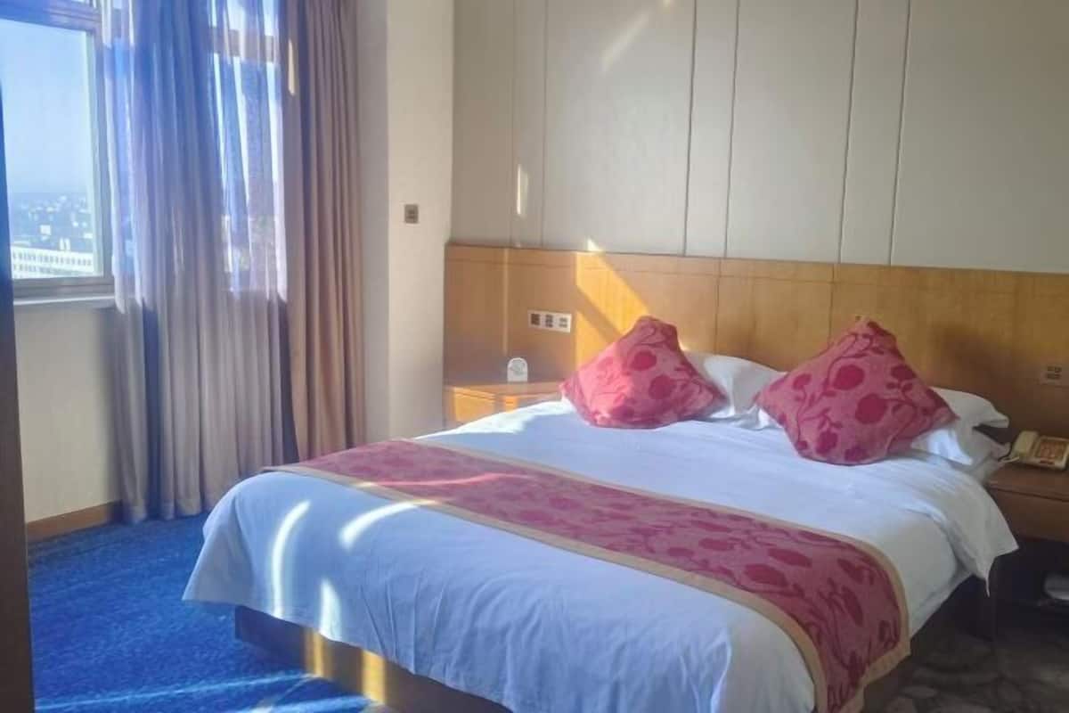 A hotel room with a large bed, a wooden headboard, a nightstand, and a window with curtains.
