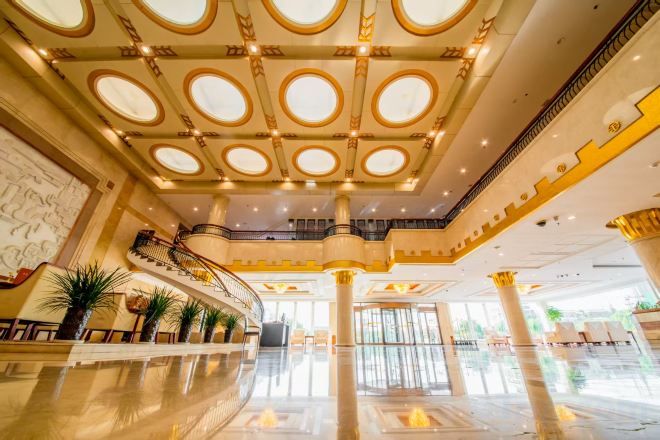 A spacious lobby with a grand staircase, large columns, and a high ceiling with circular skylights.