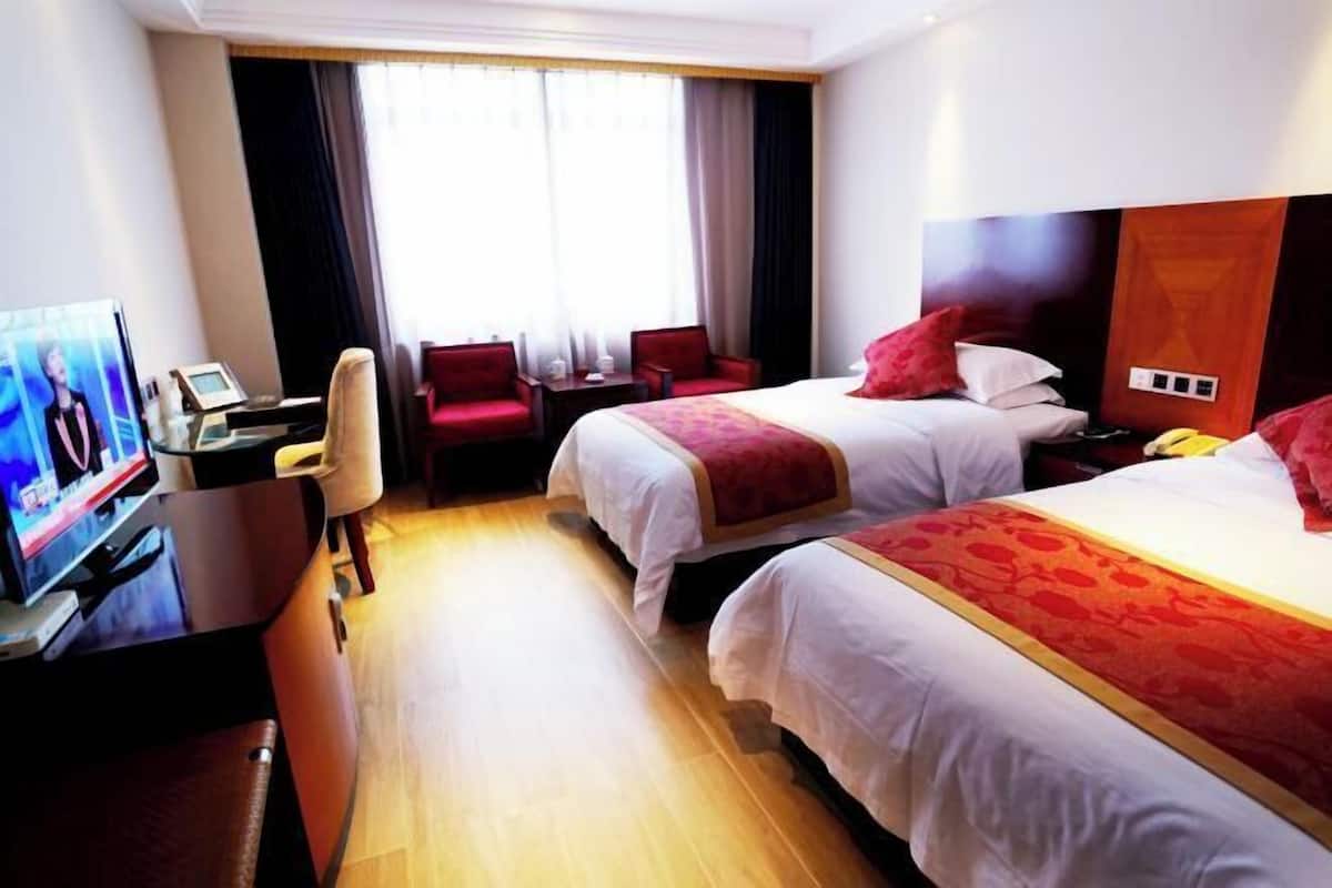 A hotel room with two beds, a desk with a television, and a window with curtains.
