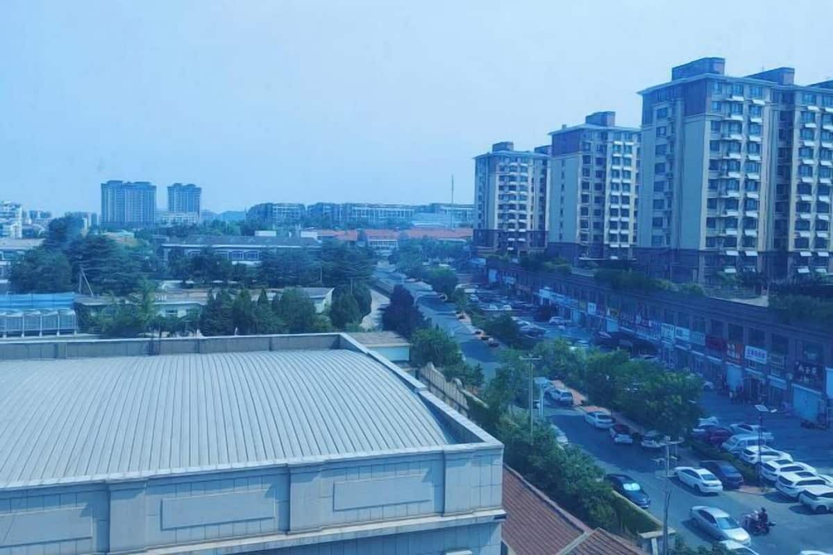 A high-rise residential building with multiple balconies, a parking lot, and surrounding low-rise buildings.