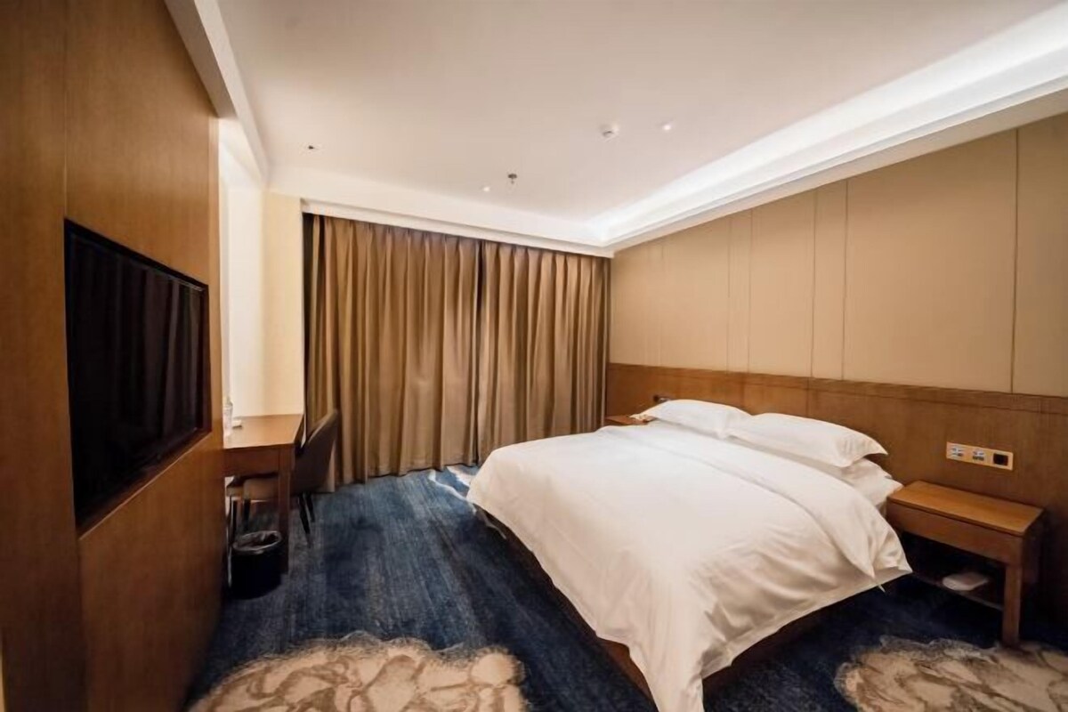 A hotel room with a bed, a TV, a wooden headboard, a nightstand, and a curtain.