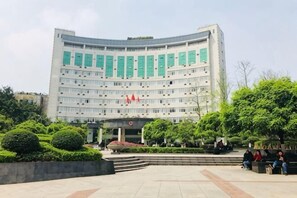 A large, multi-story building with a curved facade, a central entrance, and a landscaped courtyard with benches.