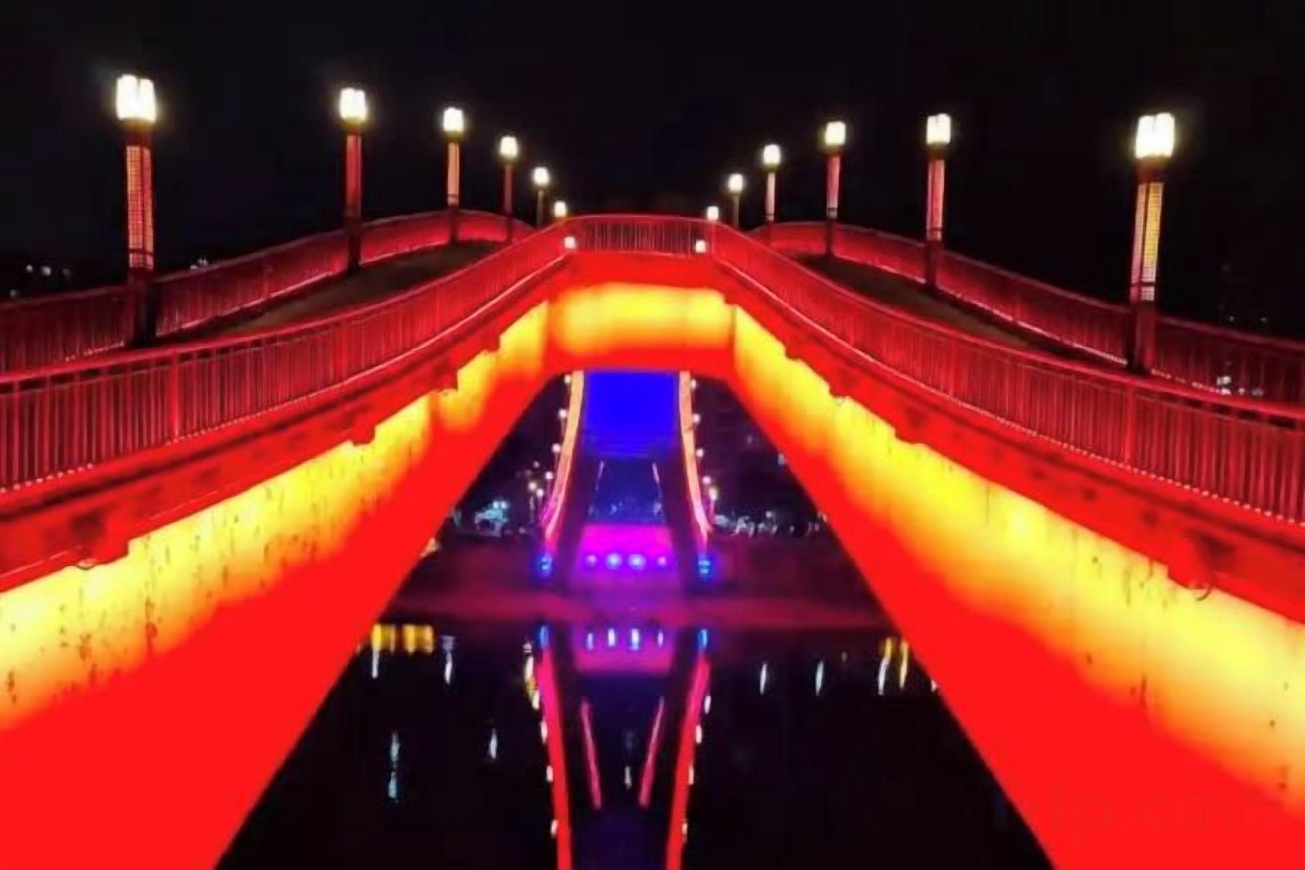 A bridge with a central pathway and railings, illuminated by street lamps.