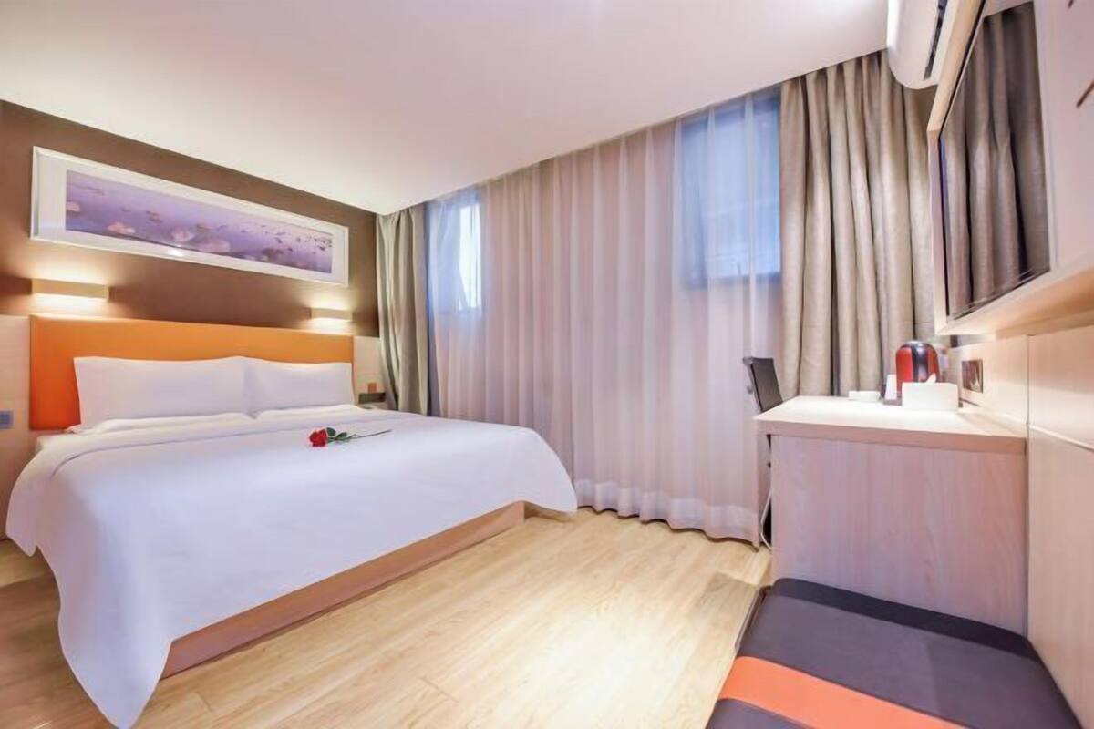 Hotellihuone, jossa on sänky, työpöytä, tuoli, ikkuna verhoilla ja taulu seinällä.