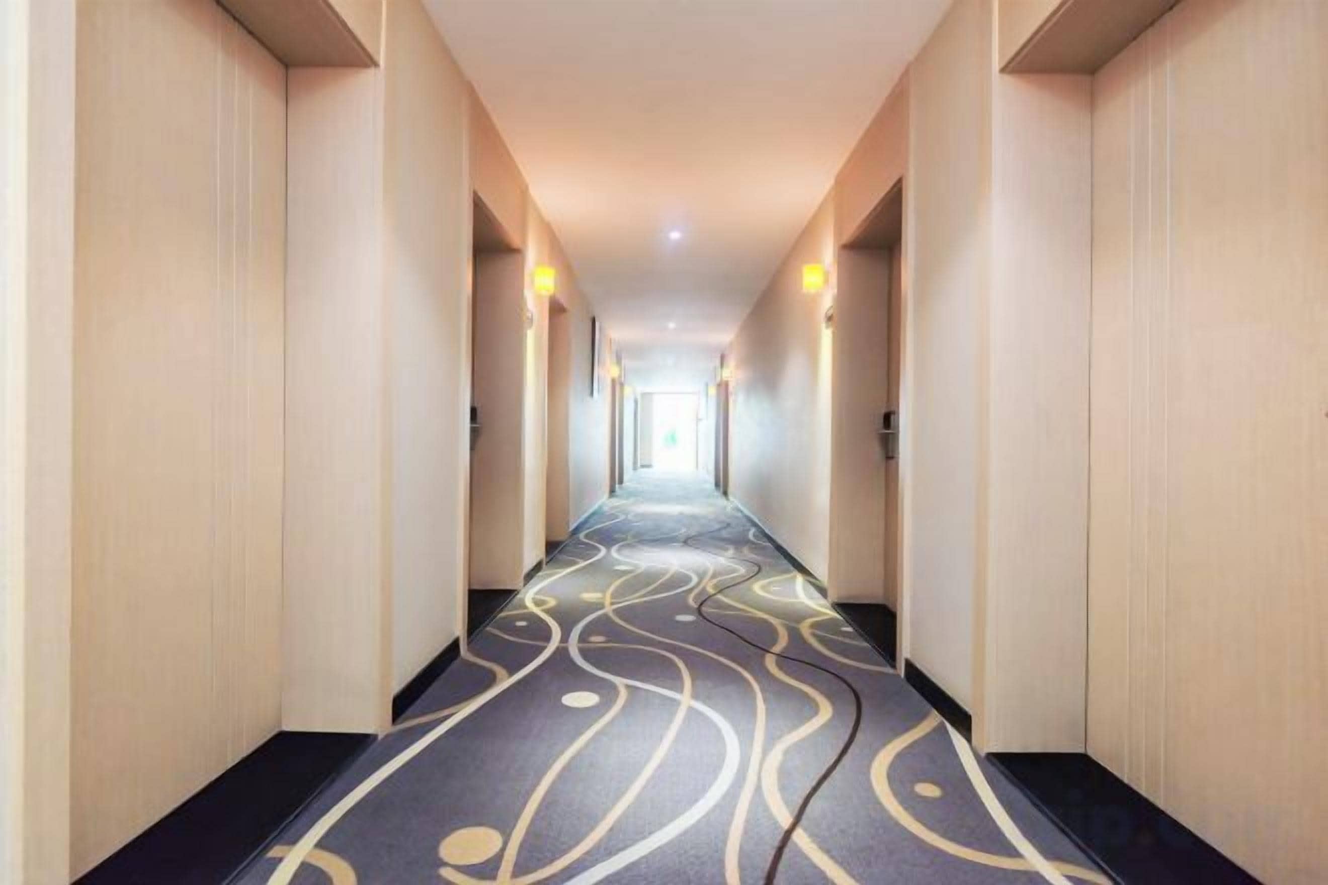 Un couloir d’hôtel avec un tapis à motifs, des murs de couleur claire et un plafond doté d’un éclairage encastré.