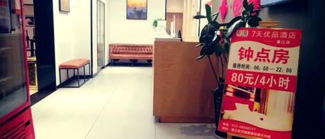 A hotel reception area with a reception desk, a bench, a television, and a welcome mat.
