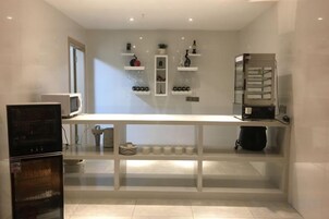 Una cocina con encimera blanca, estantes con utensilios de cocina, un microondas y un refrigerador.