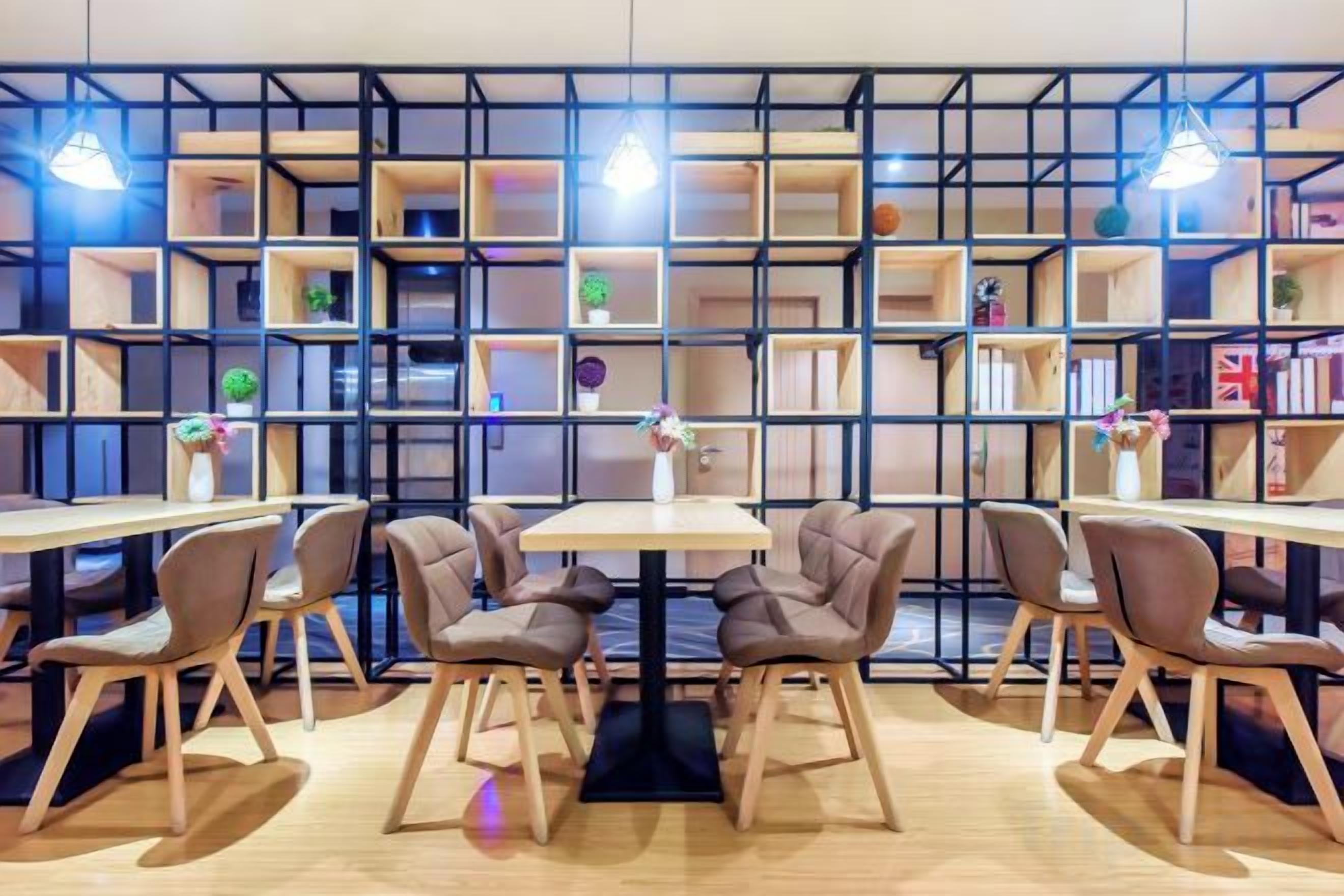 A room with a central table surrounded by chairs, a bookshelf with multiple shelves, and pendant lighting.