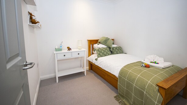 A bedroom with a bed, bedside table, and a small shelf with decorative items. - Lighthouse Lofts - Godrevy (Camborne)