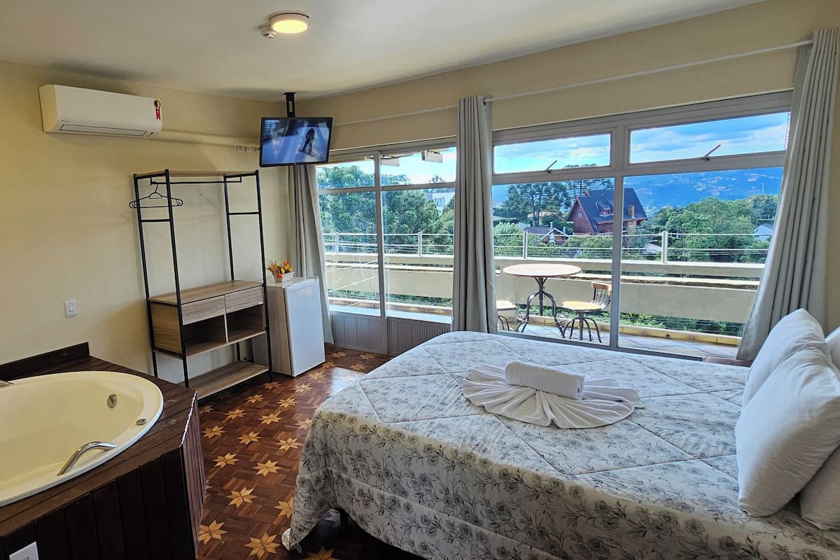 Habitación de hotel con una cama grande, baño con bañera, televisor y balcón con mesa y sillas.