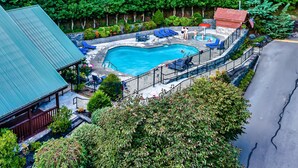 En swimmingpool omgiven av en terrass, solstolar och en liten byggnad med ett rött tak.