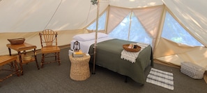Relax in a cozy tent with a comfortable bed, a small table, and a wicker stool.