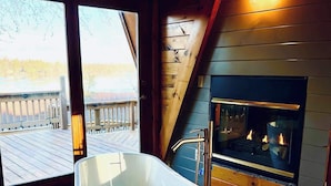 Een moderne badkamer met een vrijstaand bad, een open haard en uitzicht op een houten terras.
