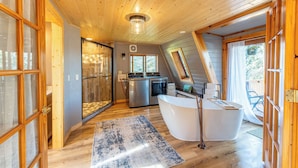 Een moderne badkamer met een vrijstaand bad, een glazen douchecabine en een houten plafond.