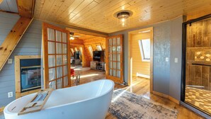 Een ruime kamer met een groot bad, houten plafond en uitzicht door openslaande deuren.