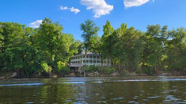 A lakeside lodge with a multi-story structure, surrounded by dense forest and reflecting on the water. - Peaceful property on the historic Suwannee River. (Bell)