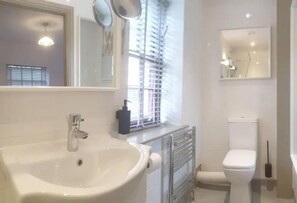 A bathroom with a white sink, a toilet, and a window with blinds. - 1700s Canalside Cottage Sleeps up to 12 Guests (Burnley)
