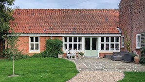A brick house with a tiled roof, a front porch with white chairs, and a gravel pathway leading to the entrance. - Soft sandy beach, award winning pub a short distance. (Ingham)