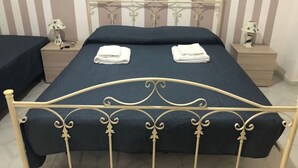 Una cama con estructura metálica y ropa de cama azul oscuro, dos toallas blancas sobre la cama y dos mesitas de noche con lámparas.