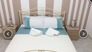 Una cama con estructura metálica, dos almohadas y dos toallas enrolladas sobre un edredón azul.