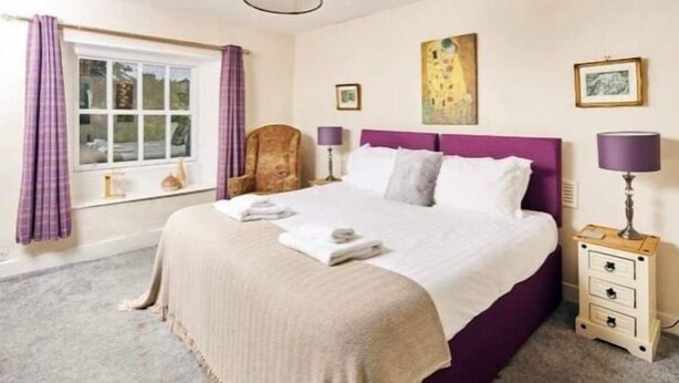 A bedroom with a large bed, a chair, a nightstand, and a window with curtains. - The Red Lion (Sedbergh)
