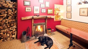 A cozy room with a fireplace, a dog lying on the floor, and a stack of firewood. - The Red Lion (Sedbergh)