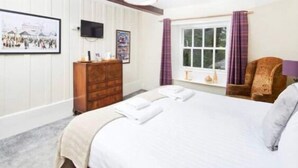 A hotel room with a bed, a wooden dresser, a television, and a window with curtains. - The Red Lion (Sedbergh)