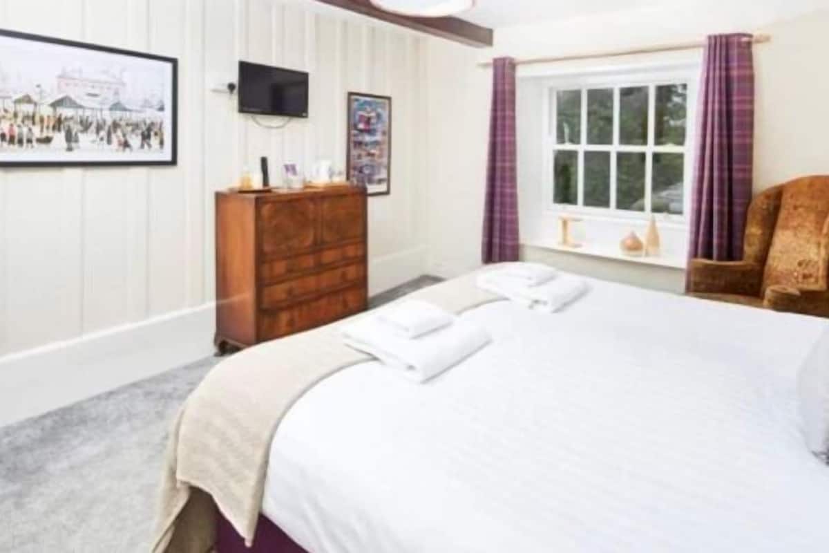 Une chambre d’hôtel avec un lit, une commode en bois, une télévision et une fenêtre avec des rideaux.
