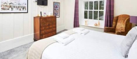 A hotel room with a bed, a wooden dresser, a television, and a window with curtains.