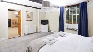 A bedroom with a bed, a TV, a radiator, a window with curtains, and a door leading to another room. - The Red Lion (Sedbergh)
