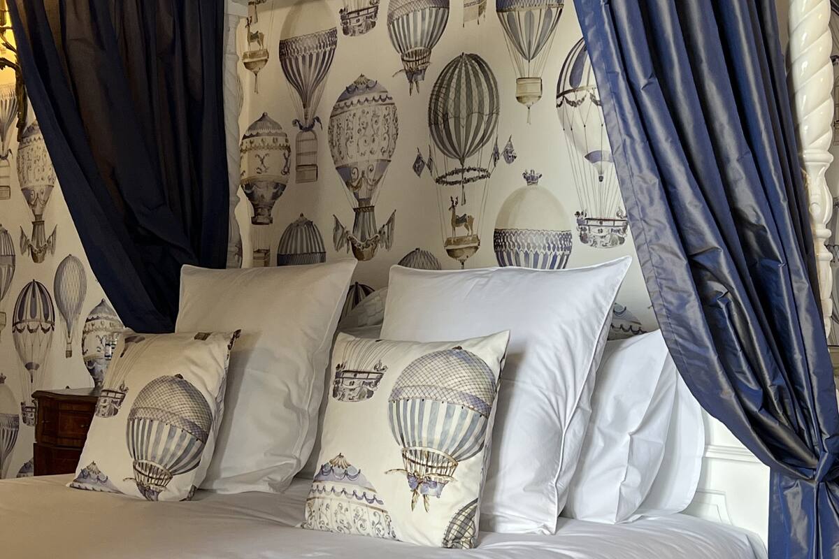 A bed with white bedding and pillows featuring hot air balloon designs, blue curtains, and a wall with similar balloon patterns.