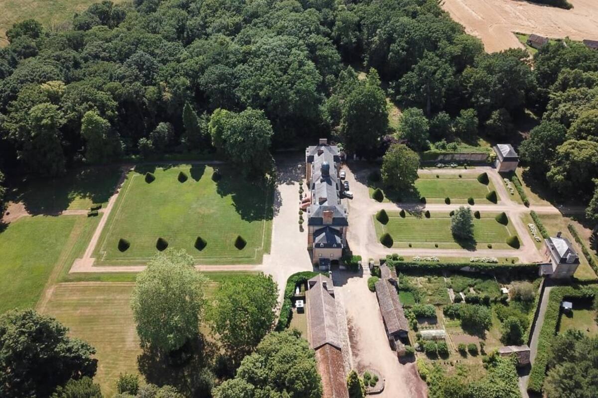 An aerial view of a large estate with multiple buildings, extensive gardens, and a well-maintained lawn.