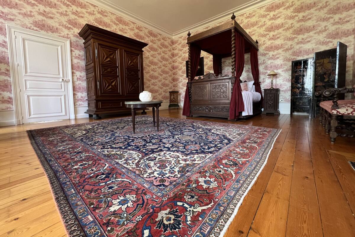 A bedroom with a four-poster bed, a large ornate wooden cabinet, and a traditional rug.
